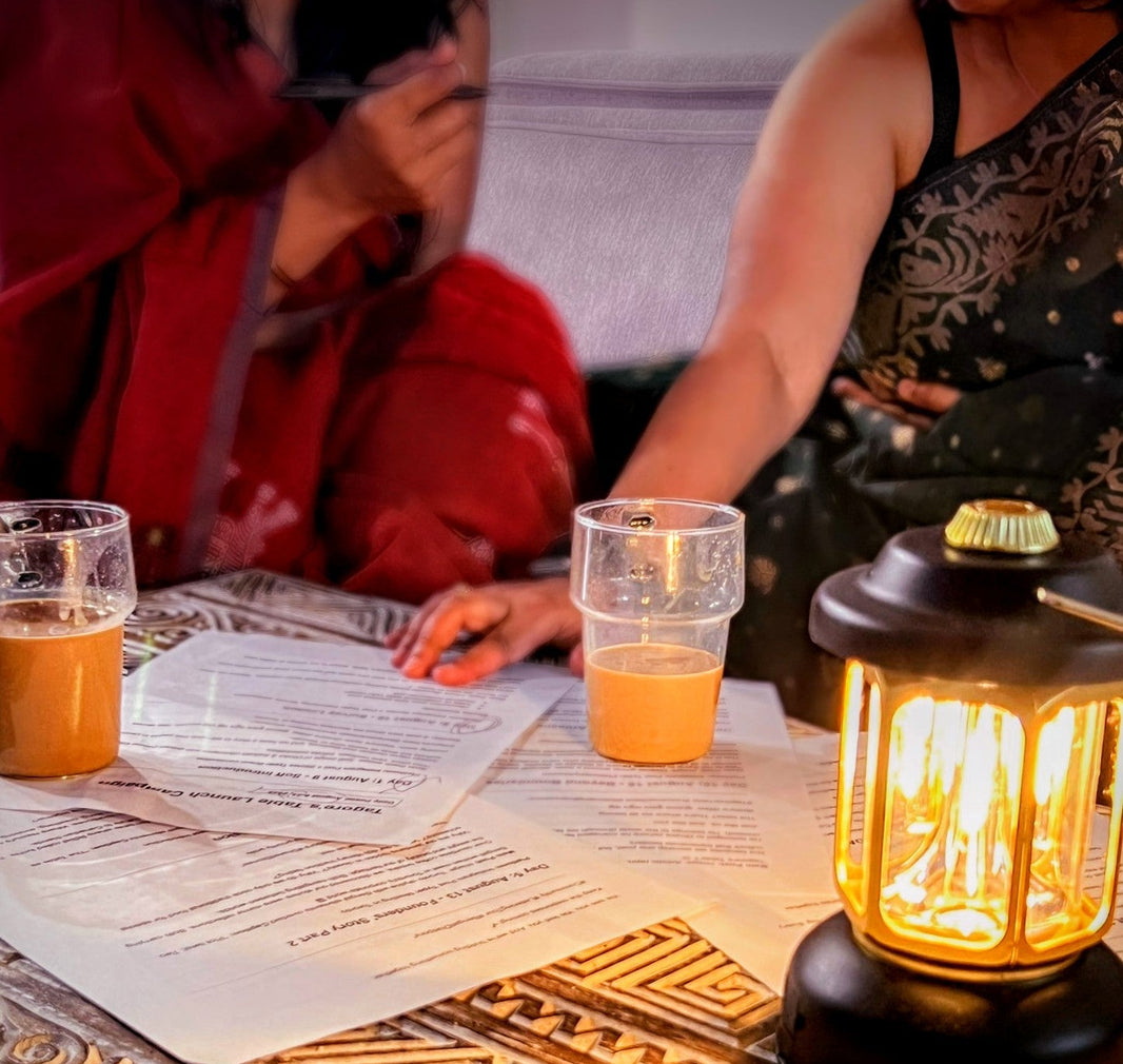 Two people sitting at a table with tea mugs and a lantern, and papers spread on a table.